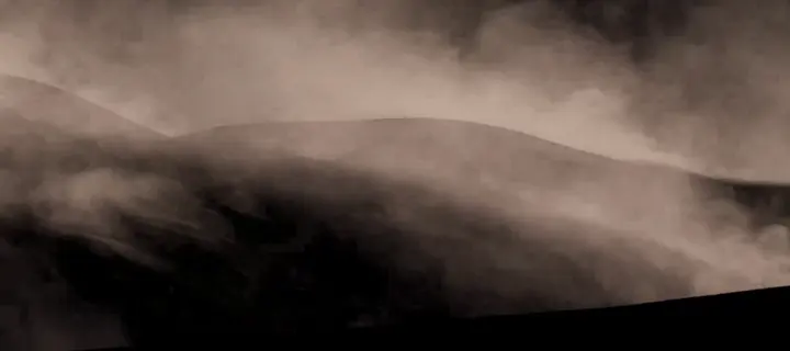 Des nuages de sable gonflés qui roulent sur une dune, sur fond noir