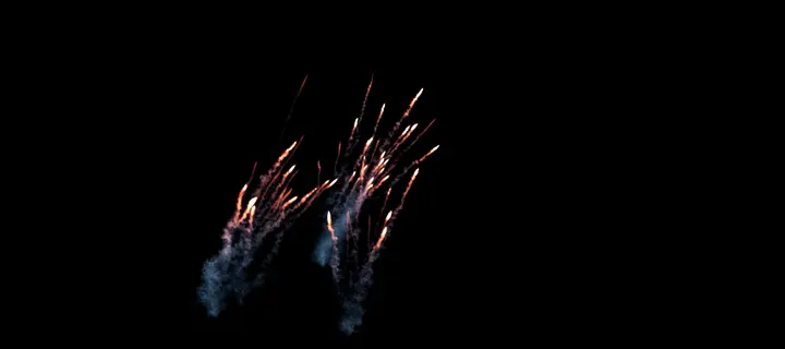 Des étincelles projetées par l’explosion, laissant des traînées de fumée bleue, sur fond noir